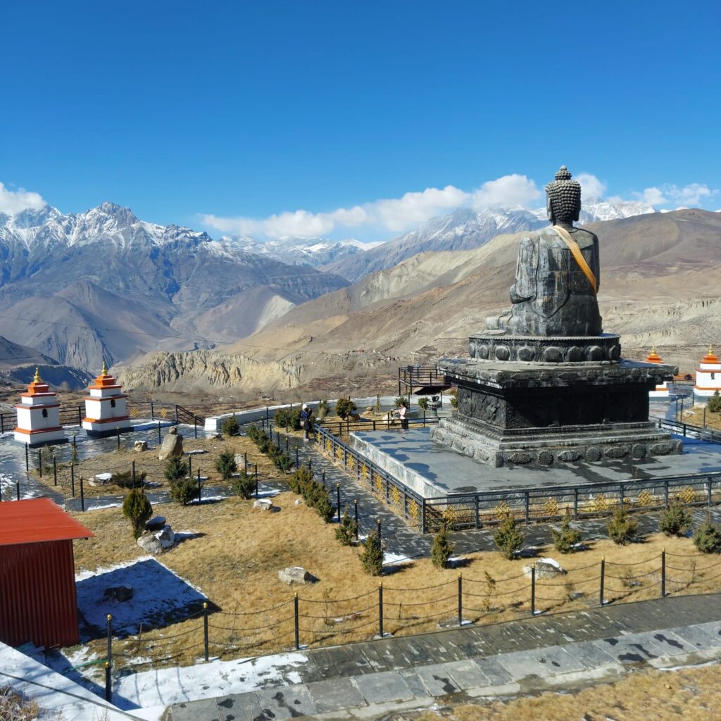 A beautifully crafted statue of Lord Buddha seated in meditation near Muktinath Temple, surrounded by prayer flags and set against the dramatic backdrop of the Himalayas. The statue symbolizes spiritual harmony and adds to the tranquil atmosphere of this revered pilgrimage site.