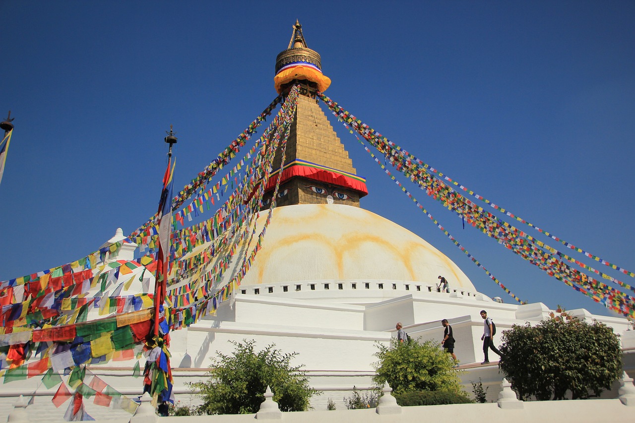 Boudhanath Stupa with its large white dome, golden spire, and colorful prayer flags under a clear sky.