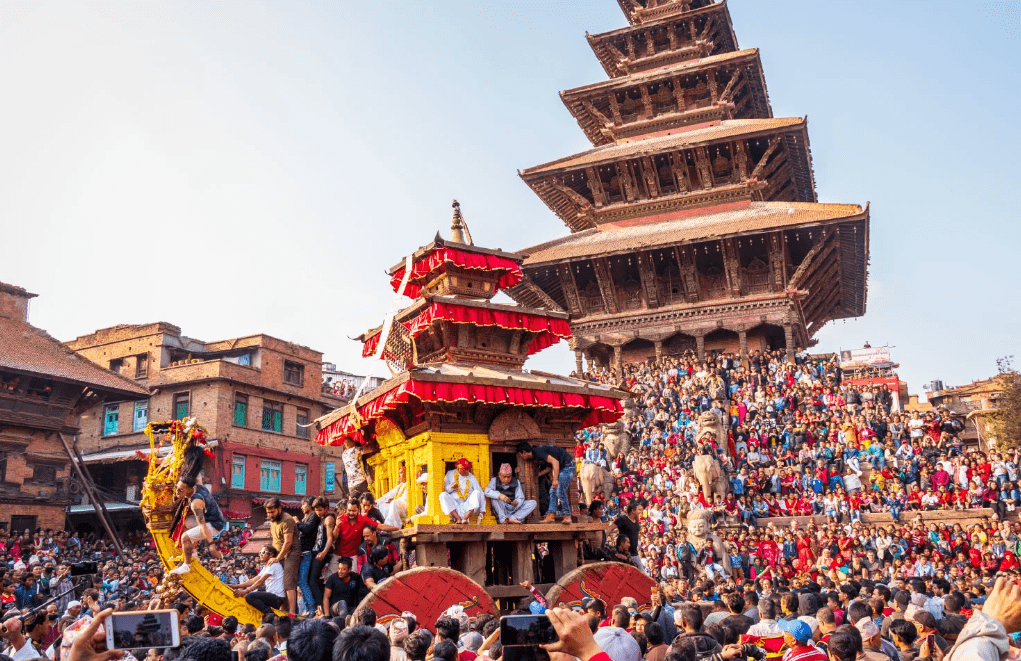 jatra-in-nepal-min People gathered and pulling a traditional wooden chariot (rath) during a Jatra festival in Nepal.