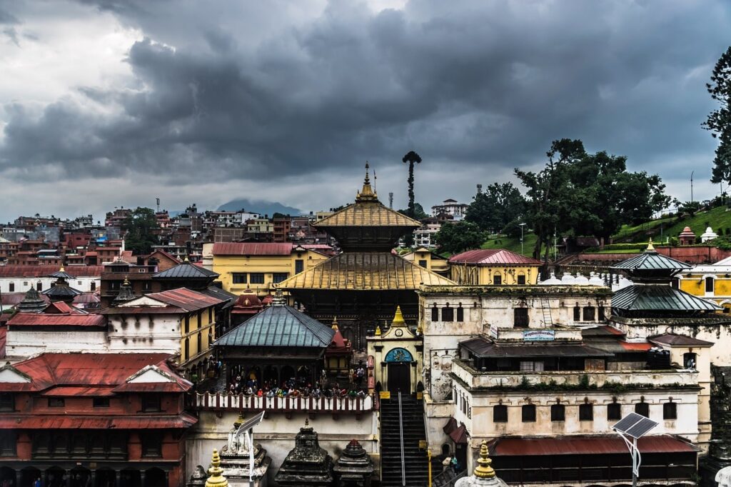 pashupatinath-temple-min A wide-angle view of the sacred Pashupatinath Temple complex in Kathmandu, Nepal, showcasing traditional pagoda-style architecture with golden rooftops and surrounding shrines.