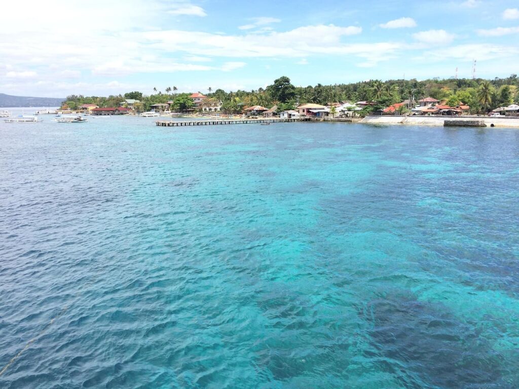 A breathtaking view of a pristine island in Cebu, Philippines, featuring crystal-clear turquoise waters and lush greenery under a bright blue sky.