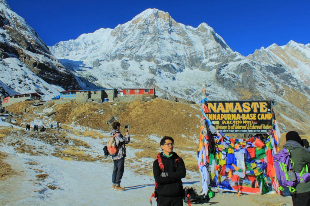 Trekkers celebrate their arrival at Annapurna Base Camp (4,130m) beneath the iconic welcome board, surrounded by towering Himalayan peaks.