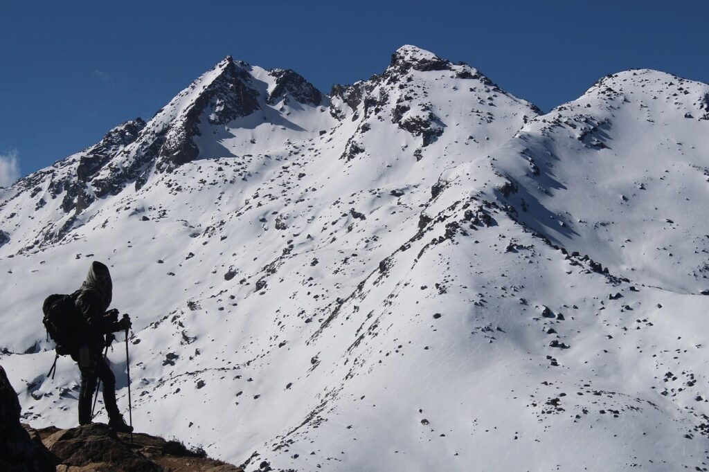 A trekker walking across Thorong La Pass, the highest point of the Annapurna Circuit, surrounded by snow-capped peaks and prayer flags fluttering in the wind.