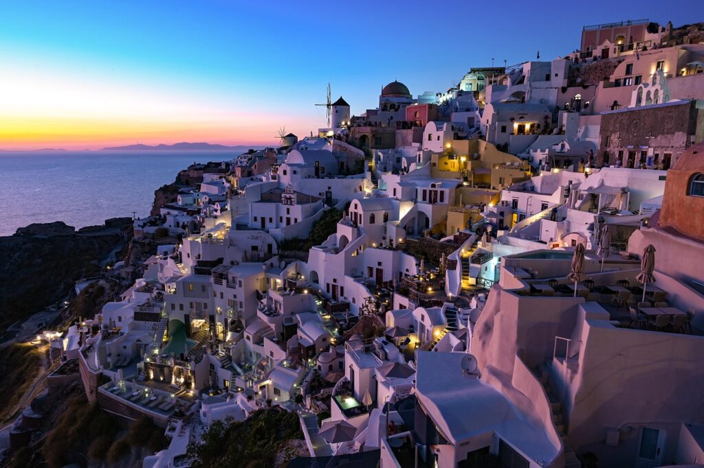 Scenic view of Santorini, Greece, featuring whitewashed buildings with blue domes perched on cliffs overlooking the deep blue Aegean Sea.