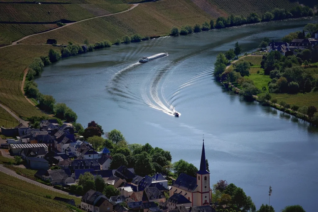 Calm river flowing through lush green landscapes in Germany, with trees lining the banks and gentle hills in the background.