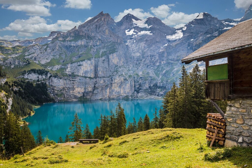 Panoramic view of a serene Swiss lake surrounded by towering snow-capped mountains and lush green forests under a clear sky.