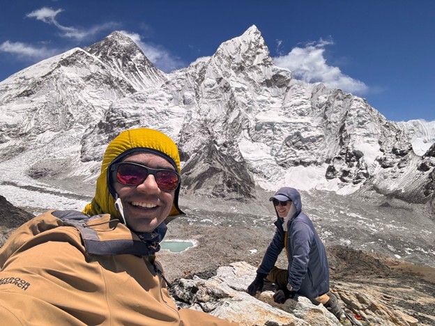 Trekker enjoying a scenic moment near Gokyo Lake with snow-capped Himalayan mountains and turquoise water in the background.