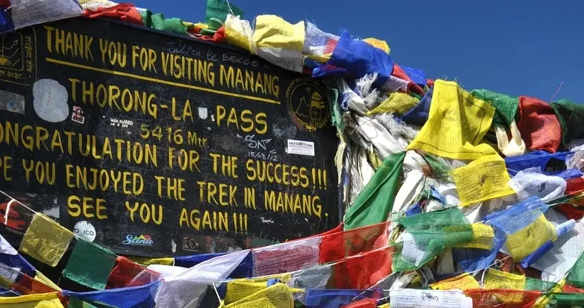 Welcome board at Thorong La Pass, marking the high-altitude trekking point in the Annapurna Circuit with surrounding snow-covered mountains and clear skies